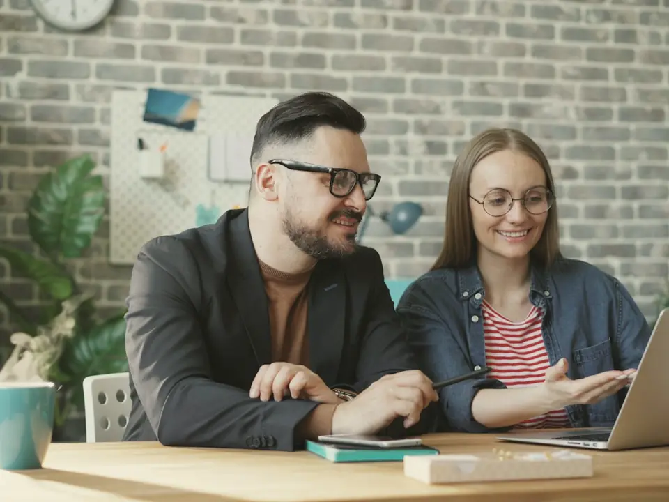 Two colleagues talking at a table over a laptop